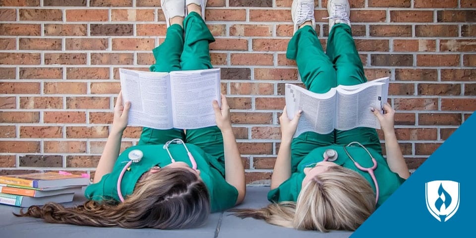 两名护士躺在人行道上读课本，脚搁在砖墙上