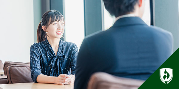 身穿深蓝波尔卡点纹衬衣的妇女坐对面与男性招聘者